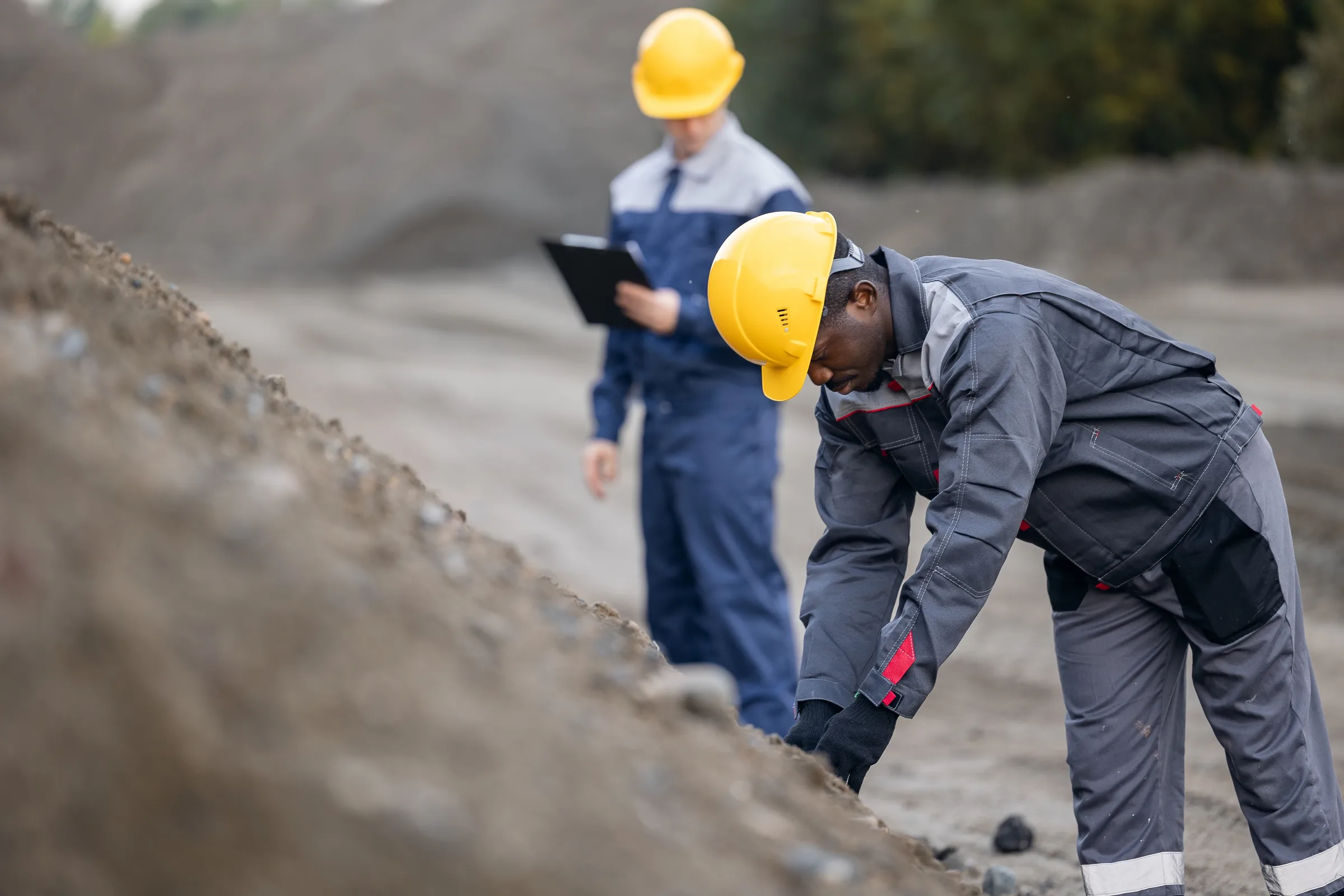 Deux travailleurs en équipement de sécurité inspectant un front de roche sur un site minier.